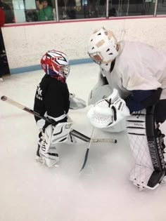 two young boys playing ice hockey on an indoor rink, one holding the goalie's helmet