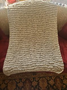 a white crocheted blanket sitting on top of a couch next to a red pillow