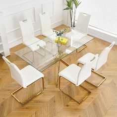 a glass dining table with white chairs and a plant in the corner on top of it