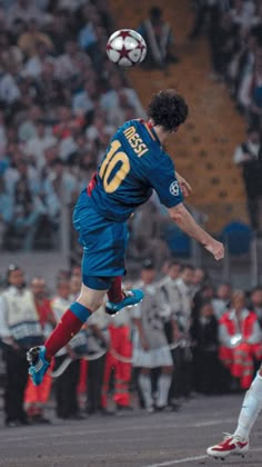 a soccer player jumps to head the ball during a game with spectators in the stands