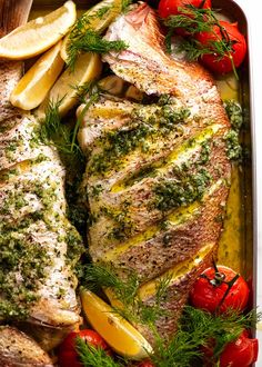 a roasting pan filled with fish, lemons and tomatoes on top of a wooden table