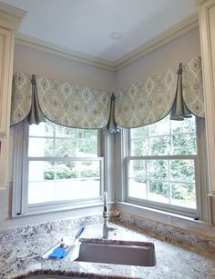 a kitchen with granite counter tops and an island in front of two windows that have roman shades on them