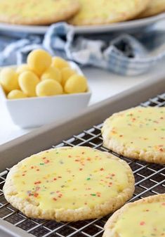 cookies with yellow icing and sprinkles on a cooling rack next to bowls of candy