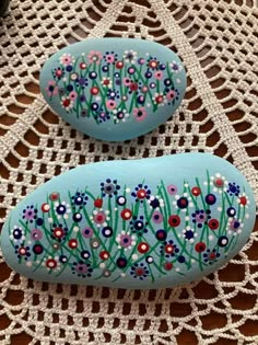 two painted rocks sitting on top of a doily covered table next to each other