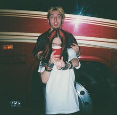 a man and woman standing in front of a red truck with their arms around each other