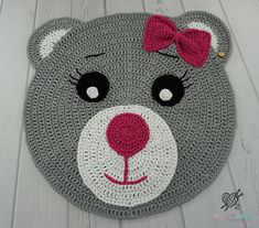 a crocheted teddy bear rug with a red bow on it's head