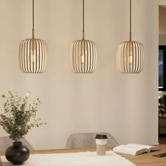 three pendant lights hanging over a dining room table with a vase and cup on it