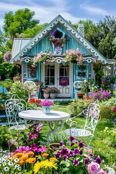 a small house with flowers around the table and chairs on the lawn in front of it