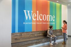 two people sitting on a bench in front of a welcome sign