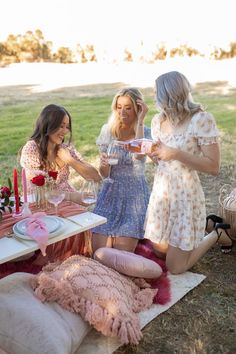 three women sitting at a picnic table with candles and flowers on the ground next to them