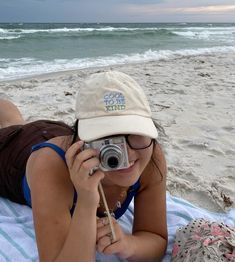 a woman laying on top of a beach holding a camera