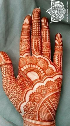 an orange henna on someones hand that is showing it's intricate designs