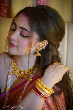 a woman wearing gold jewelry and holding onto her arm with one hand while looking down at the other