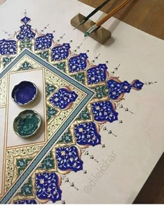 an intricately designed piece of paper with blue and green designs on it next to some paintbrushes