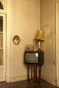 an old tv sitting on top of a wooden stand next to a lamp and door