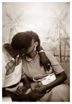 an old black and white photo of a woman kissing a man's forehead with palm trees in the background