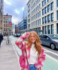 a woman standing on the side of a street next to tall buildings and parked cars