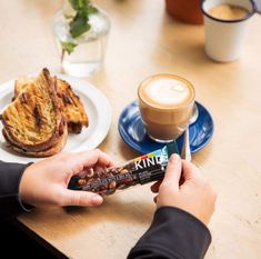 a person holding a bar next to a cup of coffee and some food on a table