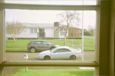 two cars parked in front of a house through a window with the reflection of another car