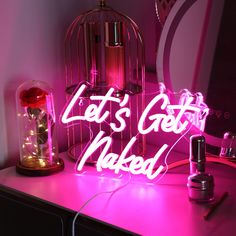 a pink neon sign that says let's get naked on top of a table