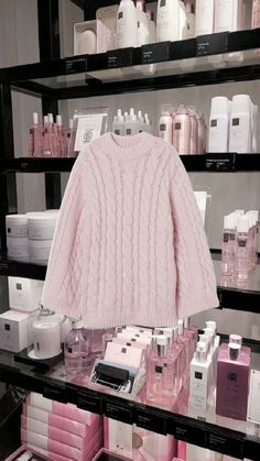 a pink sweater on display in a store with lots of bottles and boxes behind it