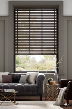 a living room with couches, chairs and windows covered in shades of brown and white