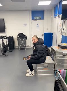 a woman sitting on top of a metal box in a room filled with luggage and other items