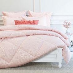 a bed with pink comforter and pillows on it in a bedroom area next to a white wall