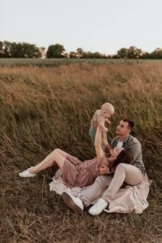 a man, woman and baby are laying on the ground in a field with tall grass