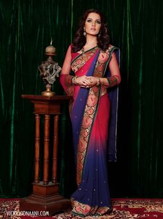 a woman in a red and blue sari standing next to a table with a vase