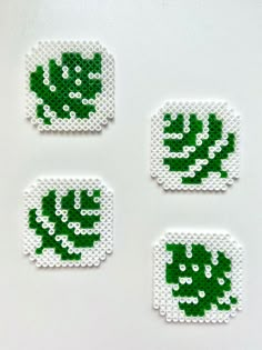 four pieces of green and white beaded artwork on a white surface, each with an image of a leaf