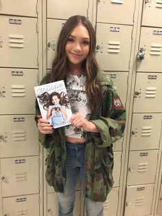 a girl holding up a book in front of lockers