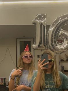 two young women taking a selfie in front of a balloon shaped like the number 20