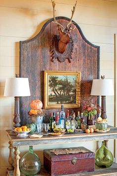 an old wooden table with bottles and glasses on it in front of a deer head