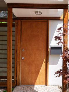 a wooden door in front of a white wall and green plants on the side walk