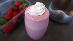 a pink drink with whipped cream on top next to strawberries