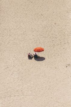 an orange umbrella sitting on top of a sandy beach