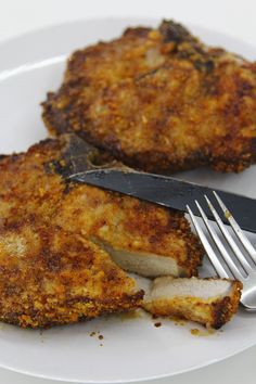 two pieces of fried chicken on a plate with a fork and knife next to it