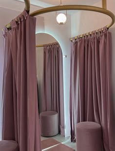 a room with pink curtains and round stools in front of a mirror that is hanging on the wall