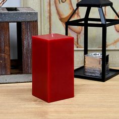 a red candle sitting on top of a wooden table next to a small black lantern