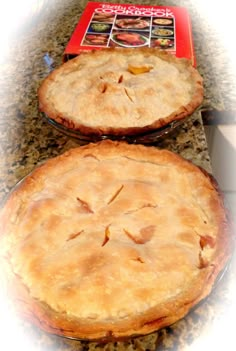 two pies sitting on top of a counter next to each other in front of a cookbook