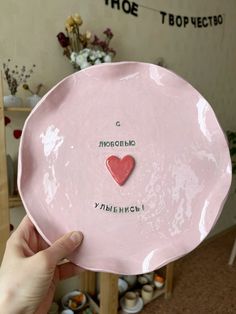 a person holding up a pink plate with a red heart on the front and words written on it