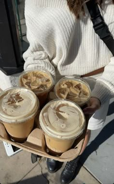 a woman holding four cups of coffee in her hands