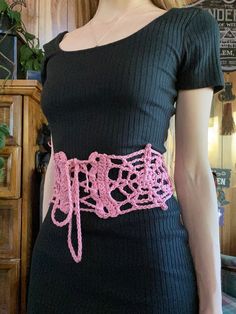 a woman wearing a black dress with pink crochet belt