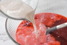 a glass bowl filled with red liquid and cream being poured into the mixture in it