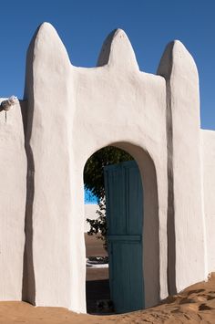 a white building with a blue door in the middle and sand on the ground behind it