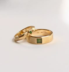 two gold wedding rings with green stones on each one and an emerald in the middle