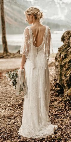 a woman in a wedding dress standing on the beach with her back to the camera