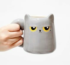 a hand holding a gray mug with yellow eyes