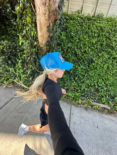 a woman riding a skateboard down a sidewalk next to a tree and shrubbery